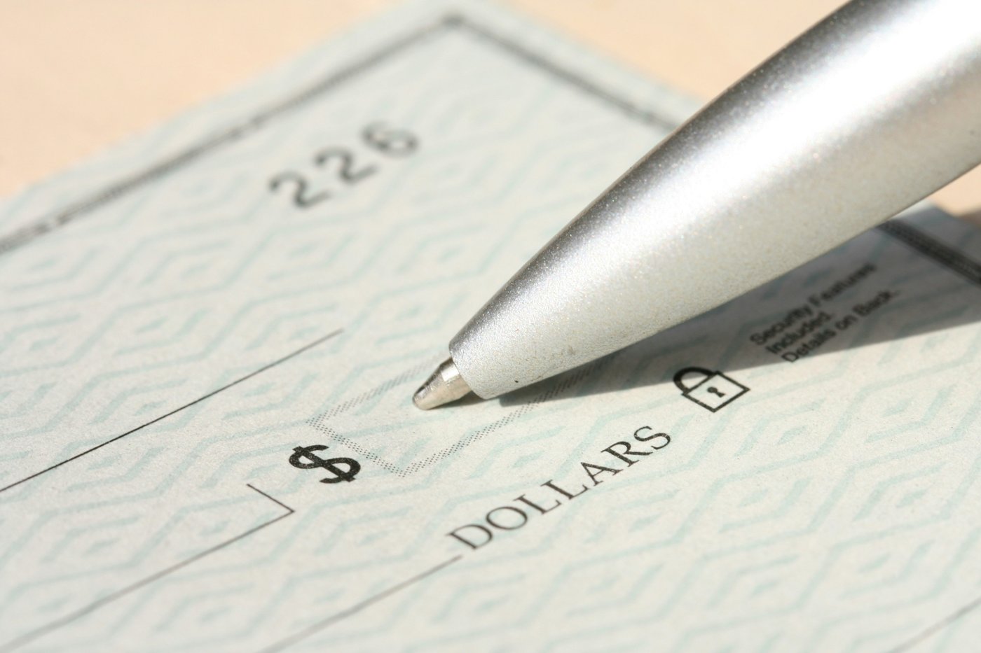 A close-up of a pen writing a check in the dollar amount field