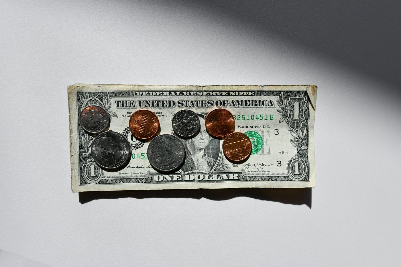 A one-dollar bill with several coins - quarters, a dime, and pennies - arranged on top of it