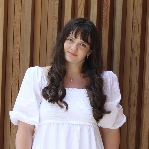 Landrey smiling in a white dress against a wood slat wall