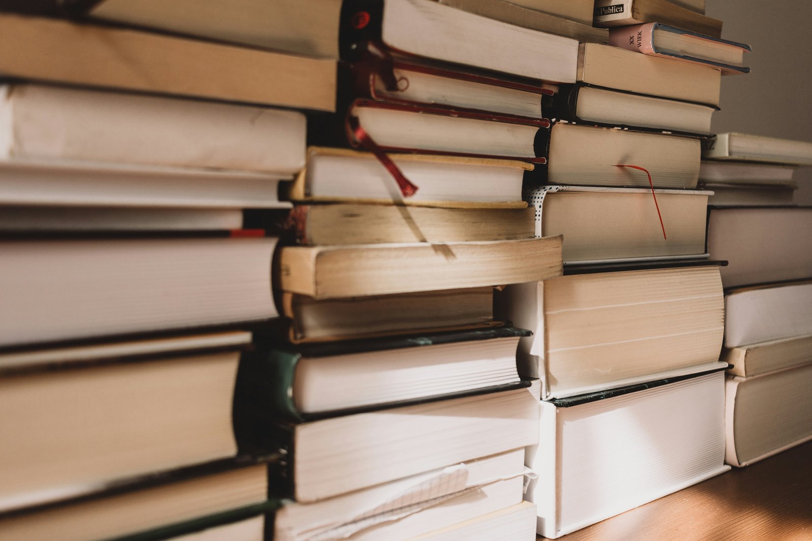 A close-up stack of hardback books with a red ribbon bookmark tucked between the pages